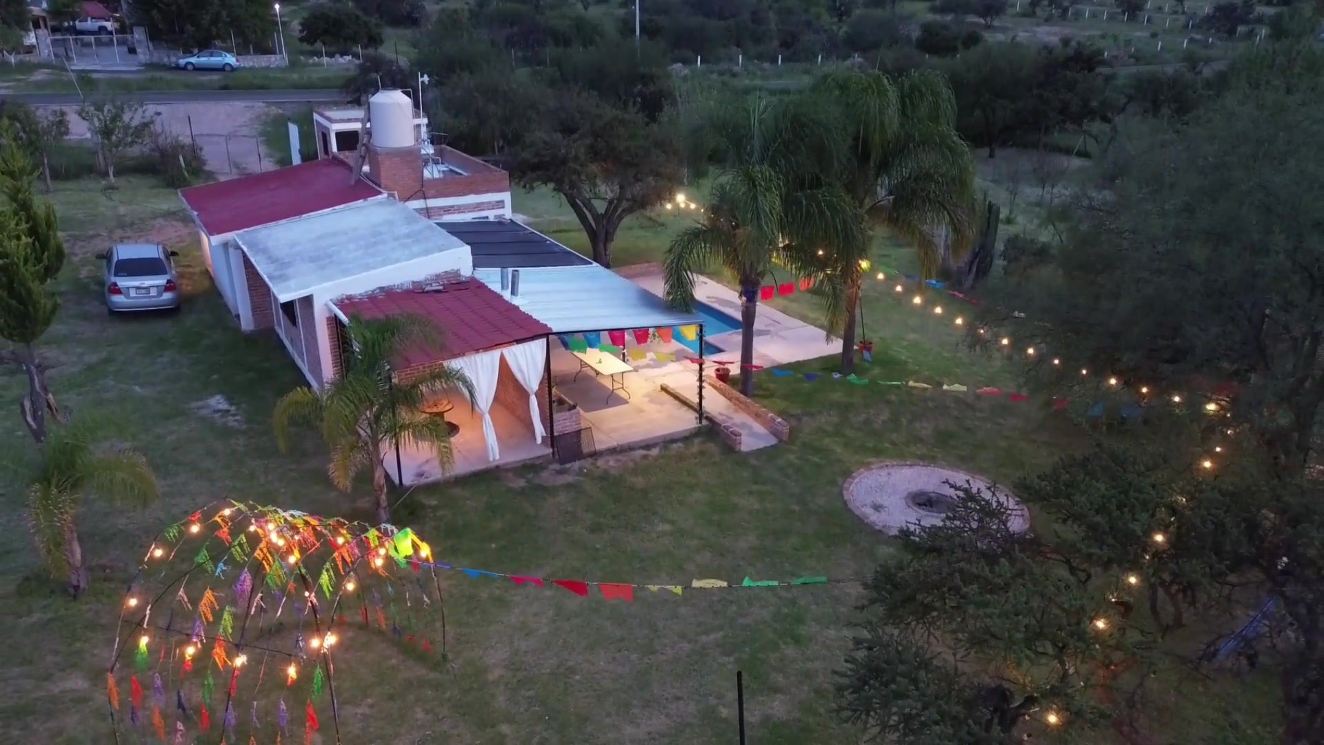 Vista aérea de Cabañas El Refugio al atardecer, con alberca, luces y fogatero